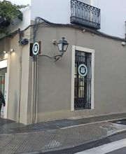 Edificio de esquina con balcones, transeúntes y autos en la calle.