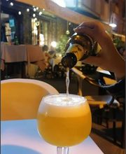 Persona sirviendo cerveza en una copa en una terraza iluminada por la noche.