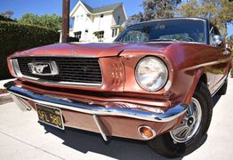 Vintage red Ford Mustang parked on a sunny street with a house in the background.