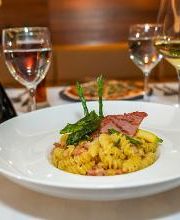 Plato de pasta con carne y espárragos sobre mesa con copas de vino y aceite de oliva.