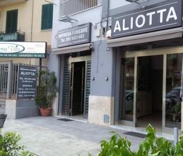 Ingresso di un'agenzia funebre "Aliotta" con cartelli e vetrine, situata su una strada cittadina.