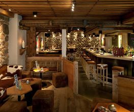 Gemütliche Bar im rustikalen Stil mit Holzmöbeln, Steinwänden und einer langen Theke.