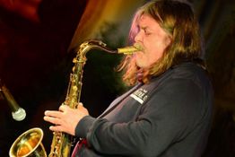 Saxophonspieler mit langen Haaren spielt leidenschaftlich Saxophon auf einer Bühne.