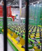 Industrielle Fertigungsanlage mit grünen Maschinen und Förderbändern hinter schwarzen Gittern.