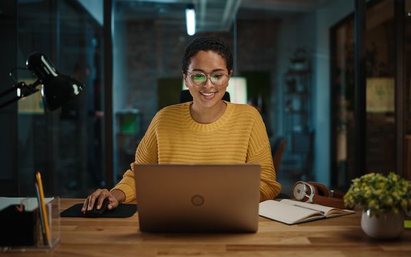 Eine junge Frau sitzt vor einem Laptop an einem Schreibtisch im Büro und baut eine One-Page Website für Ihr Start-Up Unternehmen.