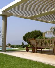 Terrasse mit Pergola am Pool, umgeben von Palmen und Rasen, mit Blick auf die Landschaft.