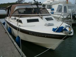 Ein Boot liegt in einem Hafen vertäut, mit blauen Fendern und brauner Abdeckung.