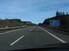 Autobahn mit blauem Schild, umgeben von Bäumen und einem klaren Himmel am Horizont.