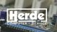 Logo von Herde.de Computer-Service auf unscharfem Hintergrund eines Computerbauteils.