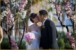 Bride and groom kiss under pink flower archway at wedding.