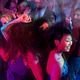 A lively group of people dancing energetically in a colorful, dimly lit nightclub.