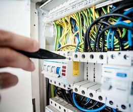 Mano con cacciavite vicino a un pannello elettrico con fili colorati.