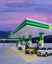 Estación de gasolina BP al atardecer, autos repostando, montañas al fondo.