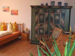 Gemütliches Zimmer mit Holzmöbeln, grünem Schrank, Bett, Holztisch und Stühlen, Pflanzen.