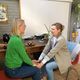 Twee vrouwen zitten tegenover elkaar en houden elkaars handen vast in een huiselijke setting.