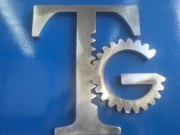 Letra "T" y "G" en metal con forma de engranaje sobre fondo azul.