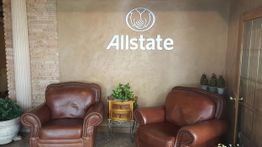 Two leather chairs in a lobby with "Allstate" logo on the wall. Plants on a small table.