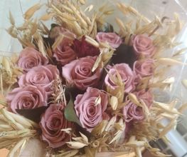 Ramo de rosas rosadas y hierbas secas envuelto en celofán transparente.