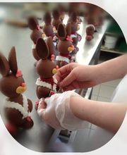 Person dekoriert Schokoladenhasen mit Schleifen auf einem Tisch.