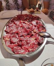Plato de carne cruda en rodajas sobre una mesa, con personas alrededor.