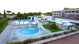 Vista dall'alto di un resort con piscine, lettini e un edificio moderno circondato dal verde.