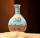 Glasflasche mit Sandmalerei: Wüste, Kamele, Berge, blauer Himmel.