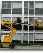 Gelber Hubsteiger steht vor einem Gebäude, Arbeiter sind in der Gondel in Höhe der Fenster.