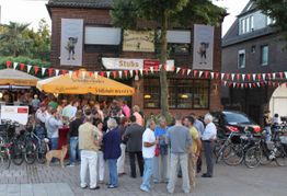 Gruppe von Menschen feiert vor einer Gaststätte mit Fahrrädern und bunten Wimpeln.