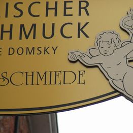 Gelbes Schild mit der Aufschrift "Schmuck" und einer Illustration eines Engels rechts.