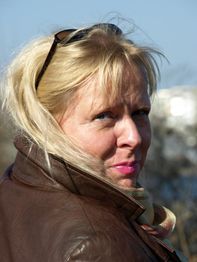 Eine Frau mit blonden Haaren und brauner Jacke schaut über die Schulter zurück.