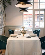 Mesa elegante en restaurante con manteles blancos, sillas verdes y lámpara moderna sobre la mesa.