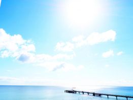 Sonniger Tag am Meer mit blauem Himmel und einem Steg im Wasser.