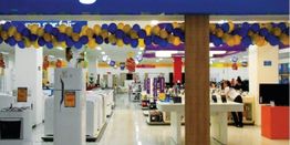 Interior de loja com eletrodomésticos e decoração em balões roxos e amarelos no teto.