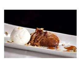 Postre en un plato: helado de vainilla junto a un pastel con salsa de caramelo y nueces.