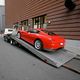 A red sports car is being loaded onto a tow truck on a city street beside a brick building.