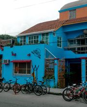 Edificio azul con bicicletas estacionadas al frente, rodeado de vegetación y cielos nublados.