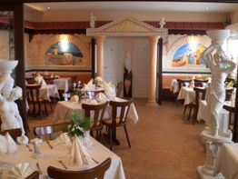 Griechisches Restaurant mit Marmorstatuen und Wandmalereien, gedeckte Tische mit weißen Tischdecken.