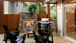 Cozy patio with stone fireplace, Adirondack chairs, and grill under wooden pergola.
