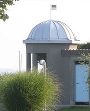 Ein Rundbau mit Kuppel, umgeben von Sträuchern und Bäumen.