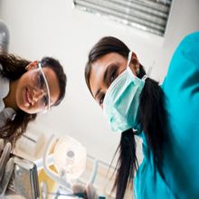 Dentists wearing masks and goggles looking down, dental equipment in the foreground.