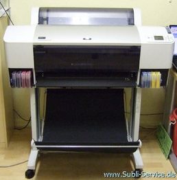 Großer Drucker auf einem Gestell, mit farbigen Tintenpatronen an den Seiten, in einem Büro.