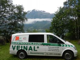 Ein weißer Van mit Werbeaufdruck, im Hintergrund Berge und Bäume.