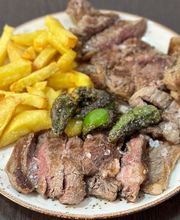 Plato de carne asada con papas fritas y pimientos verdes sobre una mesa oscura.