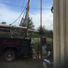 Truck with drilling equipment by a fenced area under a blue sky.