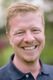 Ich kenne die Person nicht. Ein Mann mit hellem Haar lächelt in die Kamera.
