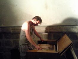 Ein Mann in einem Tanktop spielt ein geöffnetes musikalisches Instrument in einem schwach beleuchteten Raum.