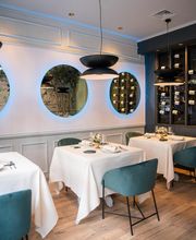 Restaurante elegante con mesas blancas, sillas azules y botellas de vino en estanterías de pared.