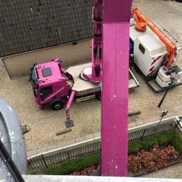 Zicht vanuit hoogte op roze en witte vrachtwagen met kraan naast gebouw.