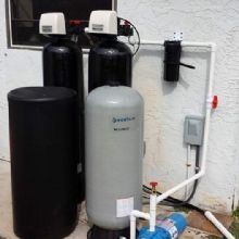 Outdoor water filtration system with two black and one gray tank connected to pipes.