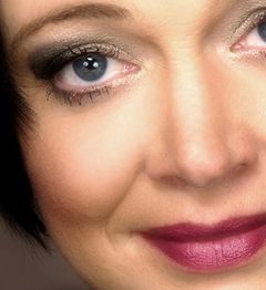 Nahaufnahme eines Frauengesichts mit blauem Auge, schwarzem Lidschatten und rotem Lippenstift.